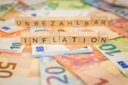 The word Inflation and Unpayable - in German for Priceless - text written in the background on banknotes Euro notes with wooden cubeの写真素材
