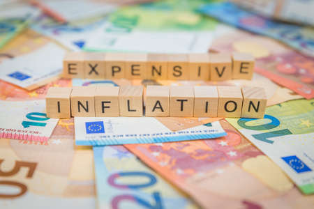 The word Inflation and Expensive in the background on banknotes Euro notes with wooden cube written textの写真素材