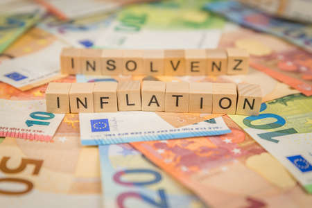 The word Inflation and Bankruptcy - in German for Insolvency - in the background on banknotes Euro notes written with wooden dice textの写真素材