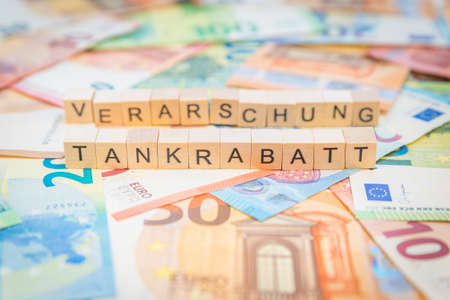 The word Tankrabatt - in German for Fuel discount - and Verarschung - in German for fooling - in the background on banknotes Euro notes written with wooden dice textの写真素材