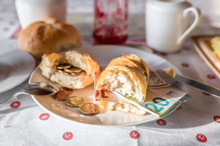 Set breakfast table with breakfast of coffee sugar milk and butter and roll covered with euro coins and banknotes on plate, Germanyの写真素材