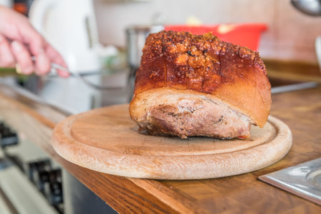 Real hearty homemade roast pork is cut into portions on a wooden board in the kitchen, Germanyの写真素材