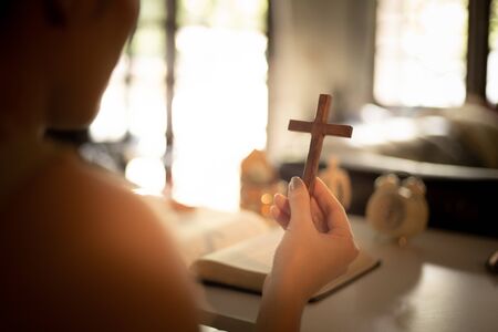 Asian woman praying and holding a cross with her bible on table. Online church from home concept.の写真素材