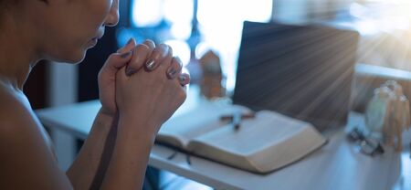 Hands praying by faith with laptop, book, notebook on it, praying position. Online church from home...