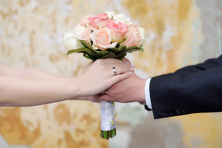 Couple hands holding a bride's bouquet over the grunge backgroundの写真素材
