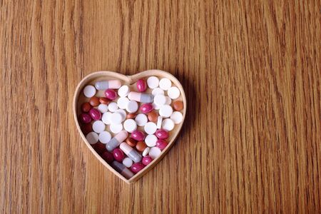 Pills in cardboard heart shape on wooden background