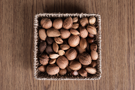 Different types of nuts in basket on wooden background