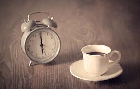 Coffee drink in vintage cup and antique clock in backgroundの写真素材