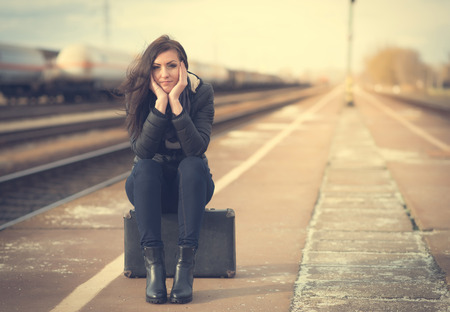 Cute woman at the train station, sitting on suitcaseの写真素材