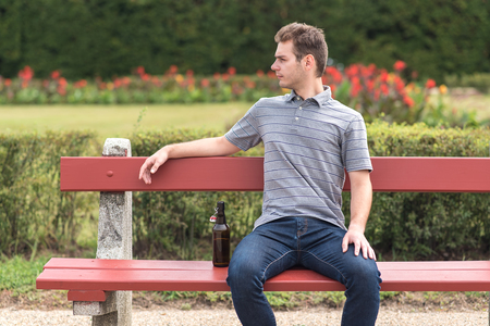 Young man sitting on bench with a bottle of beer in the parkの写真素材
