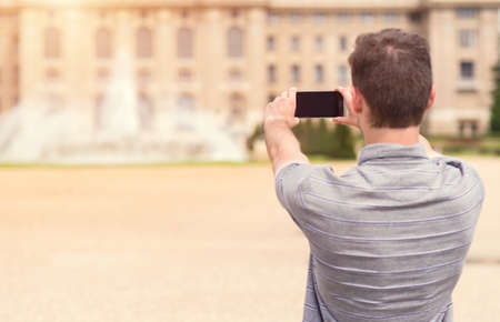 Back view of a young man tourist taking photo