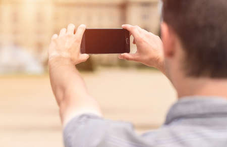 Back view of a young man tourist taking photo