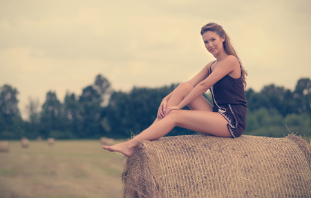 Portrait of a beautiful woman with hay bale in summerの写真素材