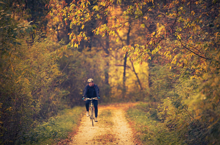 Man is bicycling in the beautiful colorful autumn forest.の写真素材