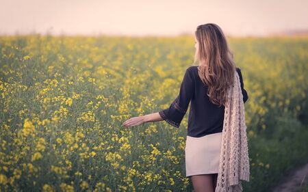 Beautiful woman walking in rapeseed field. Soft toned photo