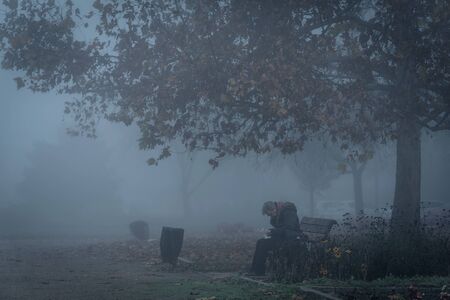 Aged homeless man sitting on a bench in the park a foggy dayの写真素材