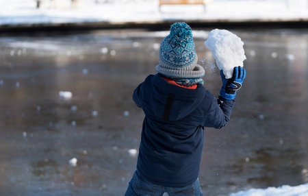 Little boy plays with snow in the park on a winter day. Throw a large snowball.の写真素材