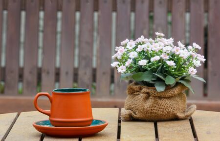 Cup of coffee and flowers on the wooden table with wooden seat in background.Focus on the cup.の写真素材