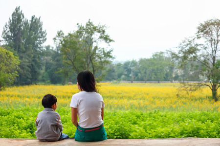 Brother and sister sit together at the yellow flower garden.の写真素材