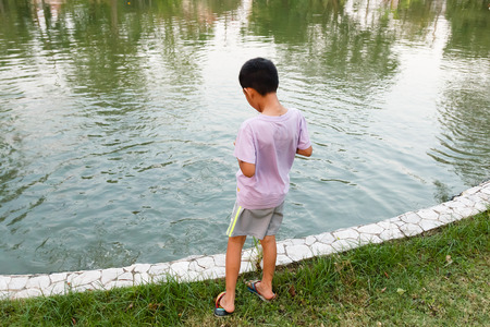 Young Thai boy feeding fish in pond.の写真素材