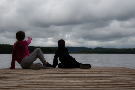 Children sitting on a dock in front of a lake in the Canadian forest in Quebecの写真素材