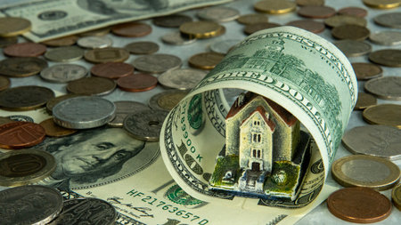 The house is wrapped in a hundred dollar bill with banknotes and coins, the concept of the real estate market, financial protection, rising housing costs, utility bills.の写真素材