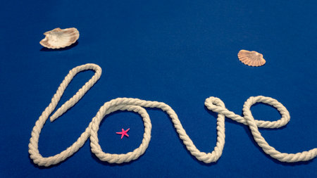 Fiber rope from which the word "love" is made with a starfish and seashells on a blue backgroundの写真素材