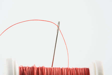 Needle and orange thread on white background