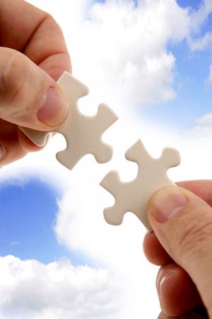 Fingers holding two puzzle pieces in front of blue sky.の写真素材