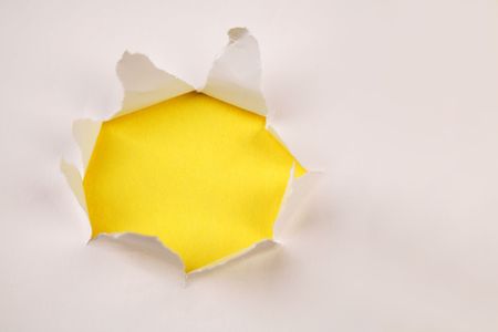 Hole ripped in paper on yellow の写真素材