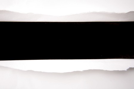 Hole ripped in white paper on blackの写真素材
