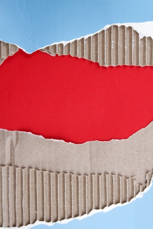 Hole ripped in corrugated cardboard on red background. Copy spaceの写真素材