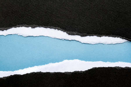 Hole ripped in black paper on blue backgroundの写真素材