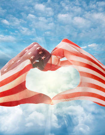 American flag on heart shaped hands, in front of bright skyの写真素材
