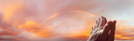 Hands together praying in rainbow skyの写真素材