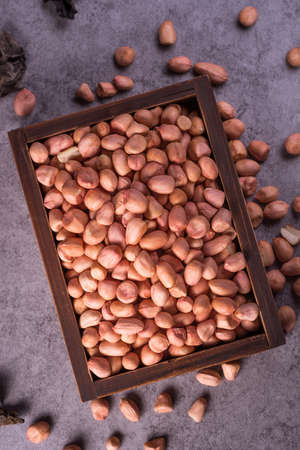 close up of raw peanuts or arachis in ceramic bowl on wood background