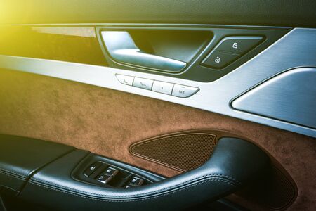 Car black perforated leather interior details of door handle with windows controls and adjustments. Car door handle inside the luxury modern car. Switch button controlの写真素材