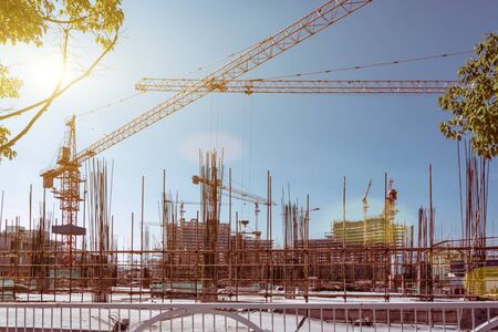 Large construction site with scaffolding building, yellow tower crane and clear blue sky.