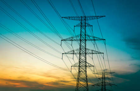 Sun setting behind the silhouette of electricity pylonsの写真素材