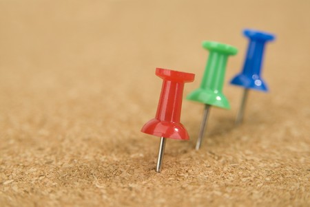 Red, green and blue push pins stuck into a cork board.