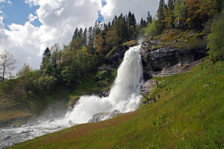 Steinsdalsfossen waterfall in the river of steine ??- scenic landscape with cascade surounded by mountains and traditional norwegian, scandinavian housesの写真素材
