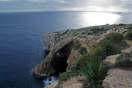 View on the sea shore with cave and cliffs in the sunsetの写真素材