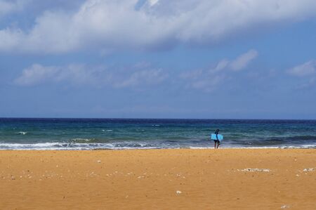 Lonely surfer on red sandy beach in Ramla Bay, Gozo, Maltaの写真素材