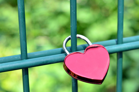 Heart-shaped padlock hangs on the bars of a fence to express eternal loveの写真素材