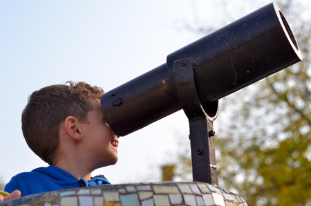 Little boy looks through binoculars on a playgroundの写真素材