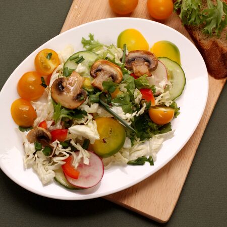 A plate of salad with vegetables, mushrooms and herbs on the table. Vegetable salad on a white dish isolated on a green background. Super food.の写真素材