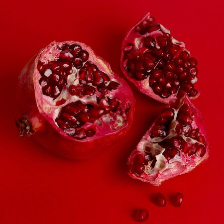 Red pomegranate isolated on red background. Pomegranate seeds on a red background. Pieces of pomegranate are scattered. Square composition. Copy space for text.の写真素材