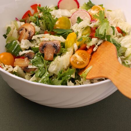A plate of salad with vegetables, mushrooms and herbs on the table. Vegetable salad on a white dish isolated on a green background. Super food.の写真素材