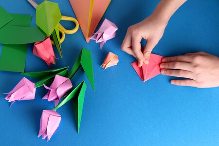 Mother's day gift. Hands of a child. Mother's Day, happy birthday, March 8, Women's Day, Valentine's Day. Bouquet of tulips from origami colored paper on a blue background. copy space.の写真素材