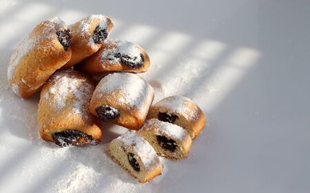 Poppy-seed cookies lie on a white table in the bright sun. Powdered sugar is sprinkled on the cookies. Beautiful shadows. Space for text.の写真素材